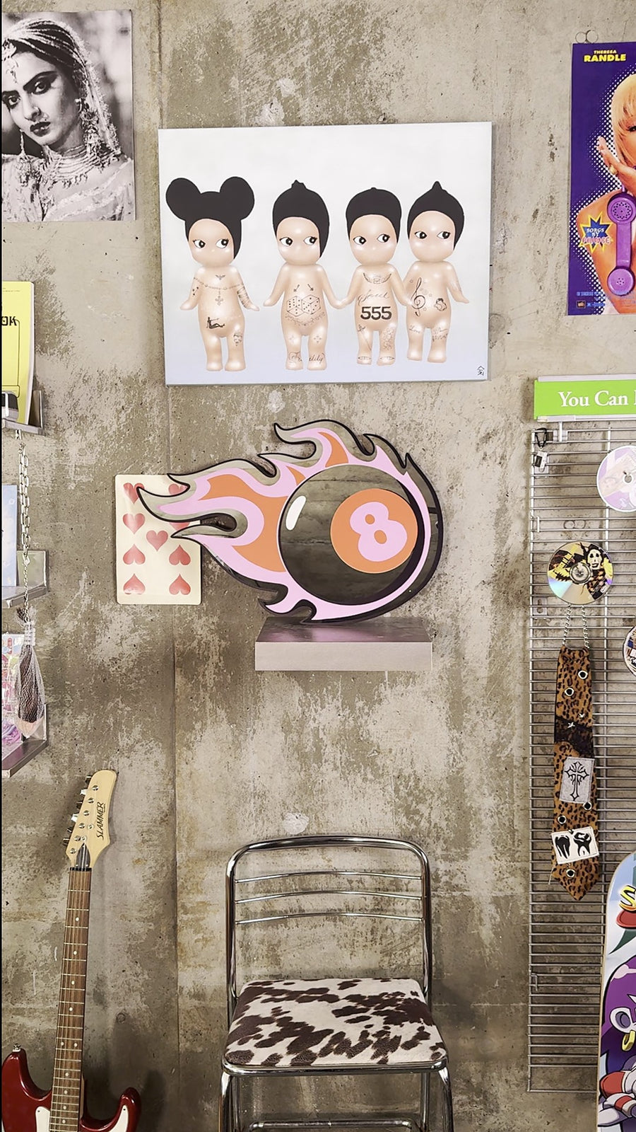 8 Ball mirror mounted on a concrete studio wall surrounded by art prints, stickers, a guitar and a cow-print chair